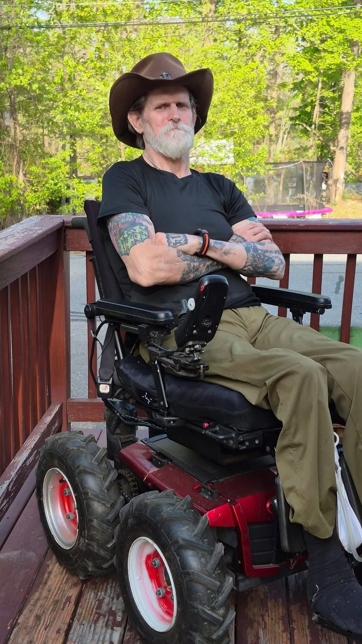 Ed Ramstrom wearing a brown cowboy hat and black T-shirt, seated outdoors with his arms crossed.