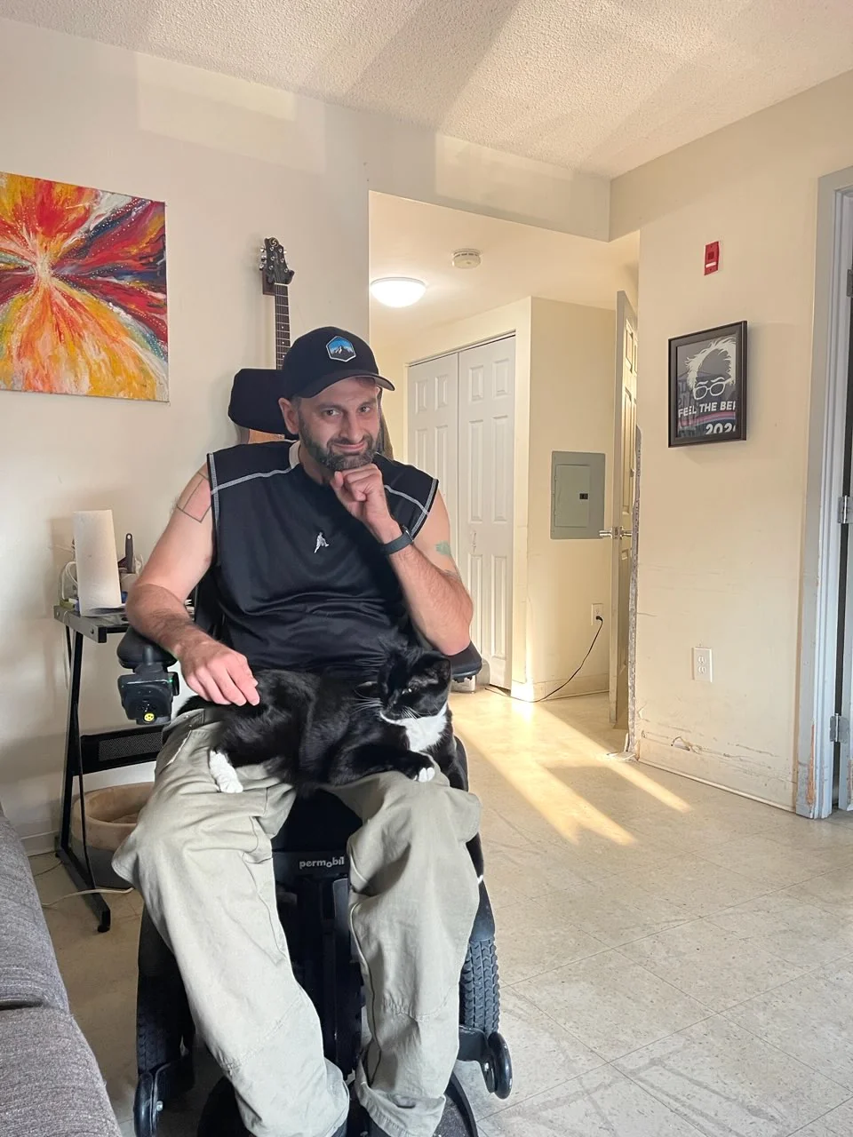 Tyler seated indoors with a black-and-white cat resting on his lap.